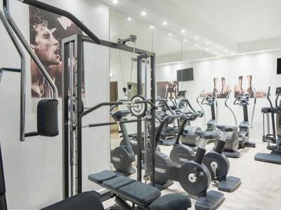 Ein heller Fitnessraum mit modernen Geräten und großen Spiegeln an den Wänden.