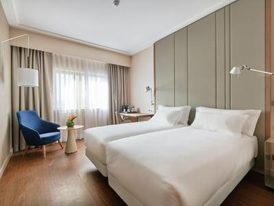 Modernes Hotelzimmer mit zwei Einzelbetten, Holzboden und gemütlichem Sitzbereich mit blauem Sessel.