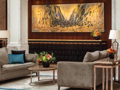 Elegante hall dell'hotel con poltrone confortevoli, tavoli rotondi e arte murale contemporanea.