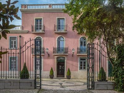 Un edificio dell'hotel rosa con cancelli in ferro battuto neri e alberi davanti.