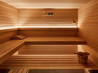 Stanza sauna con panche di legno, illuminazione e secchio di legno per l'acqua.