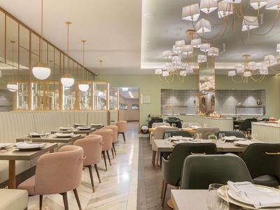 Interno di un hotel moderno con una zona pranzo elegante e comode sedie dai colori pastello.
