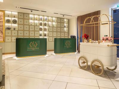 Elegante reception d'hotel con banconi verdi e carrello decorativo con composizioni floreali.