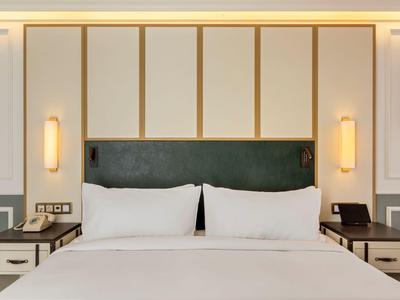 Camera d'hotel moderna con letto grande, due comodini e illuminazione calda a parete.