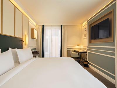Camera d'albergo moderna e luminosa con letto grande, TV e scrivania lungo la parete.