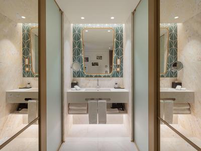 Area bagno moderna dell'hotel con doppi lavandini, grandi specchi e pareti chiare.