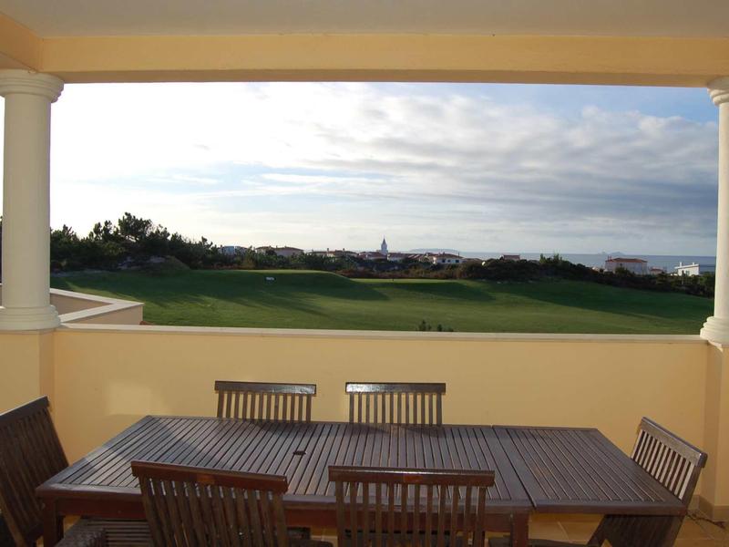 Terrazza coperta con tavolo e sedie in legno che si affacciano su un campo da golf verde.