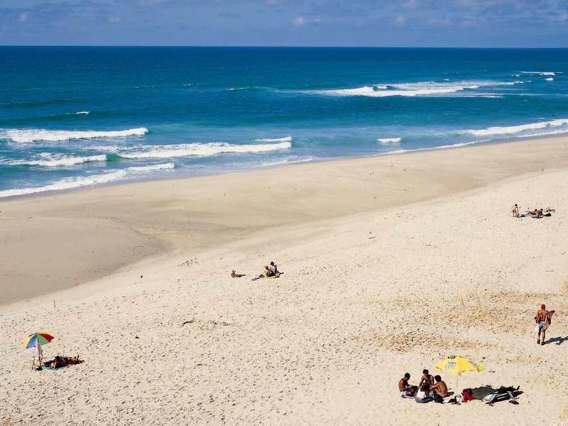 Ampia spiaggia di sabbia con poche persone e mare blu sotto un cielo sereno.