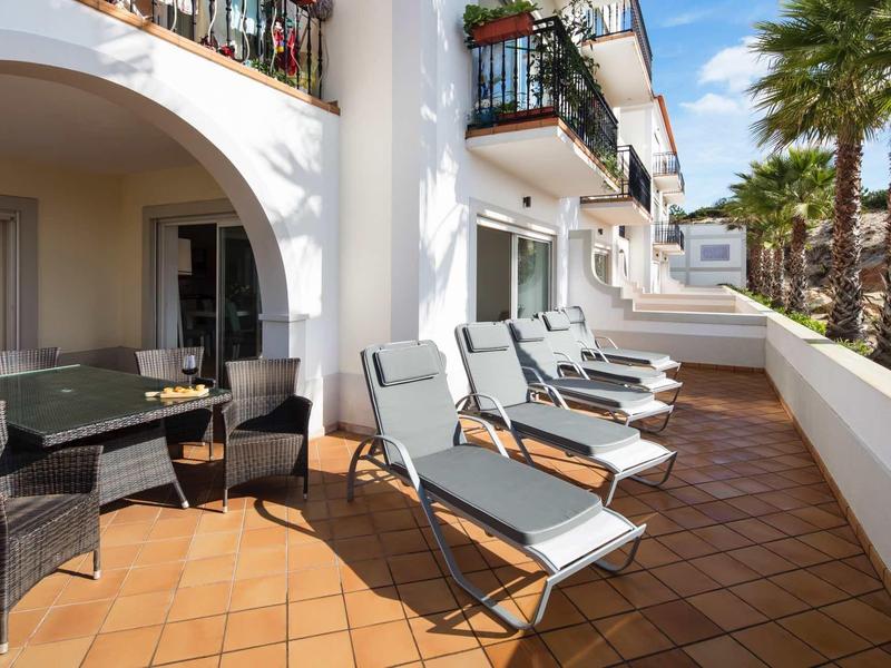 Terrazza con lettini e tavolo davanti a camere d'hotel bianche e palme.