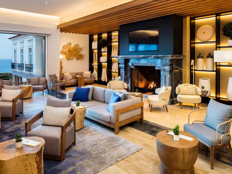 Elegante area lounge dell'hotel con poltrone, camino e vista mare attraverso grandi finestre