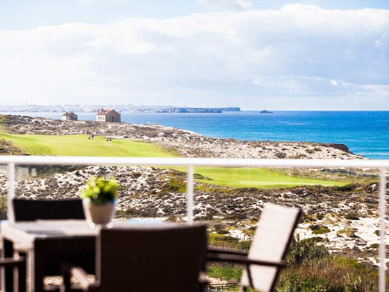 Terrazza con mobili da esterno che si affaccia su un paesaggio costiero con mare e cielo nuvoloso