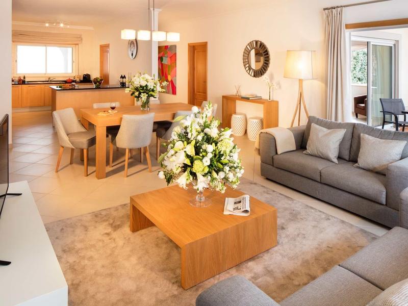 Soggiorno luminoso con divano grigio, tavolo in legno e zona pranzo adiacente con mobili in legno.