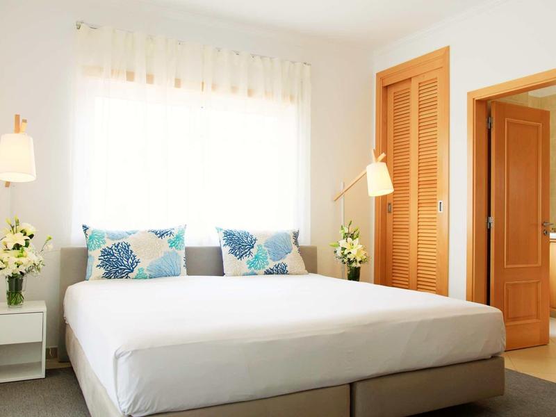 Camera luminosa con letto grande, cuscini colorati e porta verso un'altra stanza