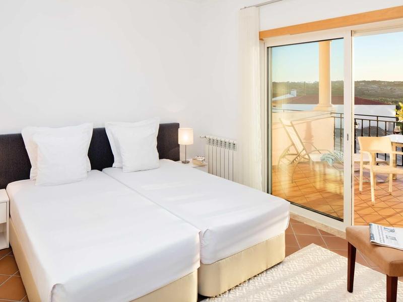 Due letti singoli in una camera luminosa con accesso al balcone e mobili da esterno.