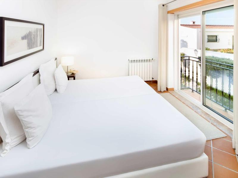 Camera luminosa con letti grandi e accesso a un balcone con vista sull'acqua.