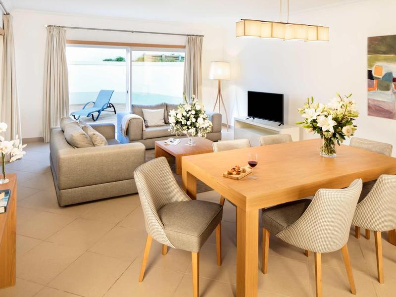 Soggiorno e sala da pranzo moderni con tavolo in legno, sedie comode e accesso alla terrazza con vista mare.