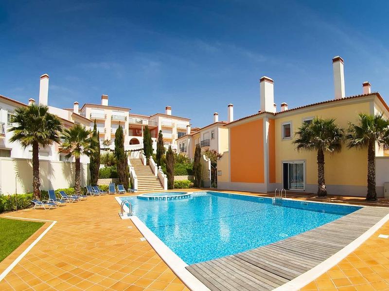 Una piscina all'aperto moderna con vasca rettangolare, circondata da edifici curati e palme.