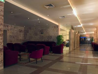 Atrio dell'hotel con zona salotto e lungo corridoio illuminato con porte e piante