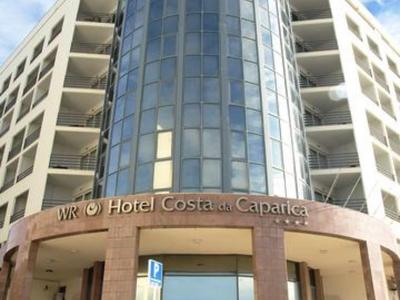 Moderner sechsstöckiger Hotelbau mit großem, runden, verglasten Eingangsturm und hellem Himmel.