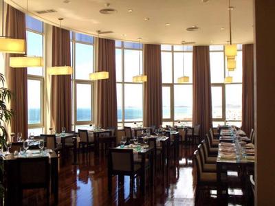 Helles Restaurant mit großen Fenstern, braunen Vorhängen und gut gedeckten Holztischen.