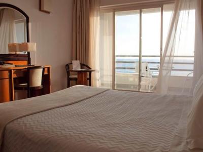 Hell eingerichtetes Schlafzimmer mit großem Bett, Tisch, Stühlen und Balkon mit Glasfassade.