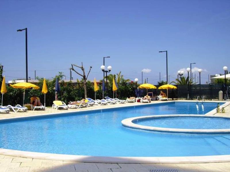 Großer Außenpool mit klarem Wasser, gelben Sonnenschirmen und Liegestühlen unter blauem Himmel.