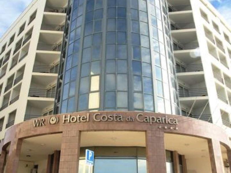 Moderner sechsstöckiger Hotelbau mit großem, runden, verglasten Eingangsturm und hellem Himmel.