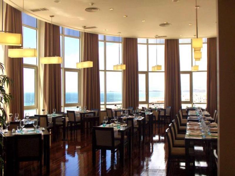 Helles Restaurant mit großen Fenstern, braunen Vorhängen und gut gedeckten Holztischen.