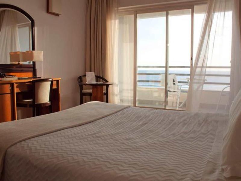 Hell eingerichtetes Schlafzimmer mit großem Bett, Tisch, Stühlen und Balkon mit Glasfassade.