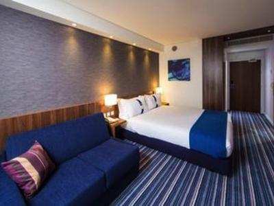 Moderne hotelkamer met tweepersoonsbed, blauwe bank en gestreept tapijt.