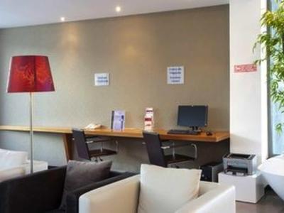 Moderne hotel lounge met computers, stoelen en een rode vloerlamp tegen de muur.