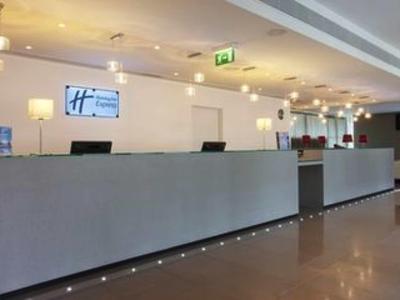 Helle Hotellobby mit langem grauem Empfangstresen, Sitzecke und mehreren Deckenlampen.