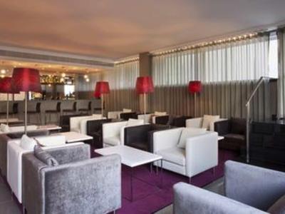Moderne hotel-lounge met witte fauteuils en rode lampen bij zacht licht.