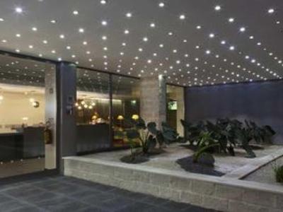 Moderne hotelentree met plantenarrangementen en heldere plafondverlichting.