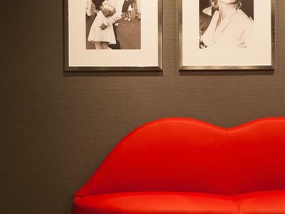Red lips-shaped sofa against gray wall with two black and white photos in white frames.