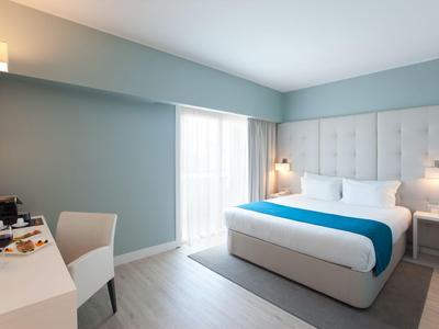 Modern hotel room with large bed, desk, and window with curtains.