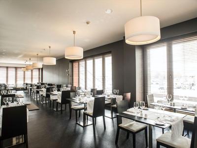 Modern restaurant with stylish wooden tables and chairs beside large windows.