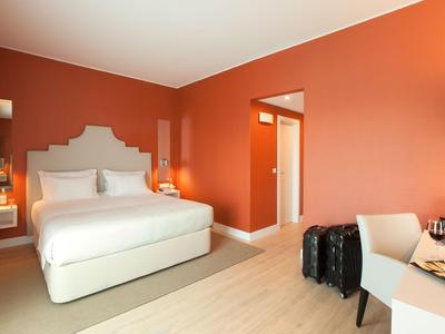Modern hotel room with orange walls, large bed, and desk with seating area.