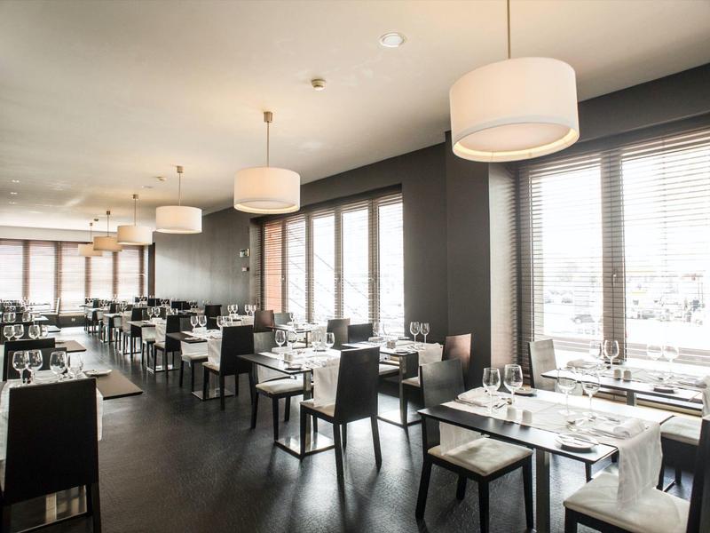 Ristorante moderno con tavoli eleganti, sedie e grandi finestre che lasciano entrare la luce del giorno.