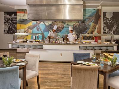 A chef prepares dishes in a modern hotel kitchen with set tables in the foreground.