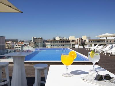 Una terrazza sul tetto con piscina, lettini e un tavolo con cocktail sotto un cielo blu limpido.