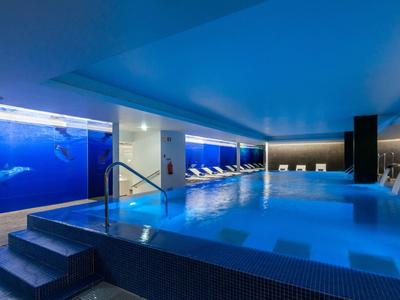 Piscina coperta moderna con pareti blu, lettini e illuminazione rilassante.