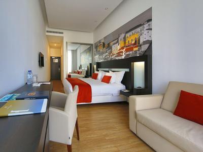 Modern hotel room with double bed, red accents, sofa, and desk.