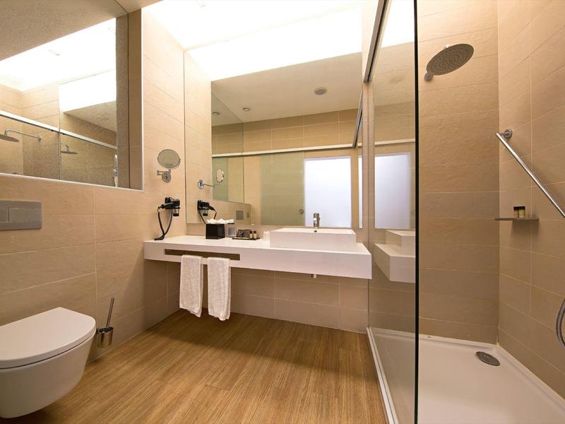 Bagno moderno dell'hotel con doccia, toilette e lavabo in tonalità calde beige e marroni.