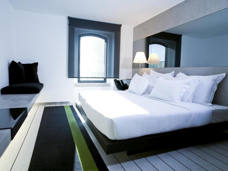 Camera d'hotel moderna con letto grande, finestra e interni semplici bianchi e grigi.