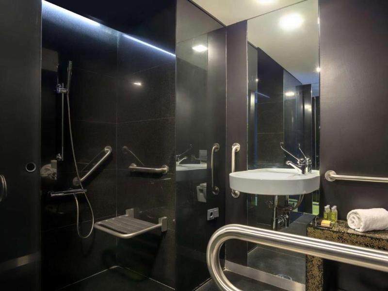 Bagno accessibile moderno con piastrelle scure, specchio a parete, lavabo e sedile doccia.