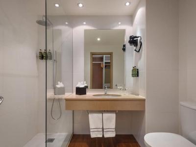 Modern, lichte badkamer met douche, wastafel, spiegel en toilet in een hotelkamer.