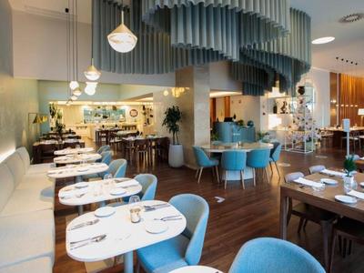 Modern restaurant met witte tafels, blauwe stoelen en elegant gebogen plafondontwerp.