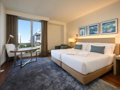 Modern hotelkamer met twee eenpersoonsbedden, tapijtvloer en balkon met zeezicht.