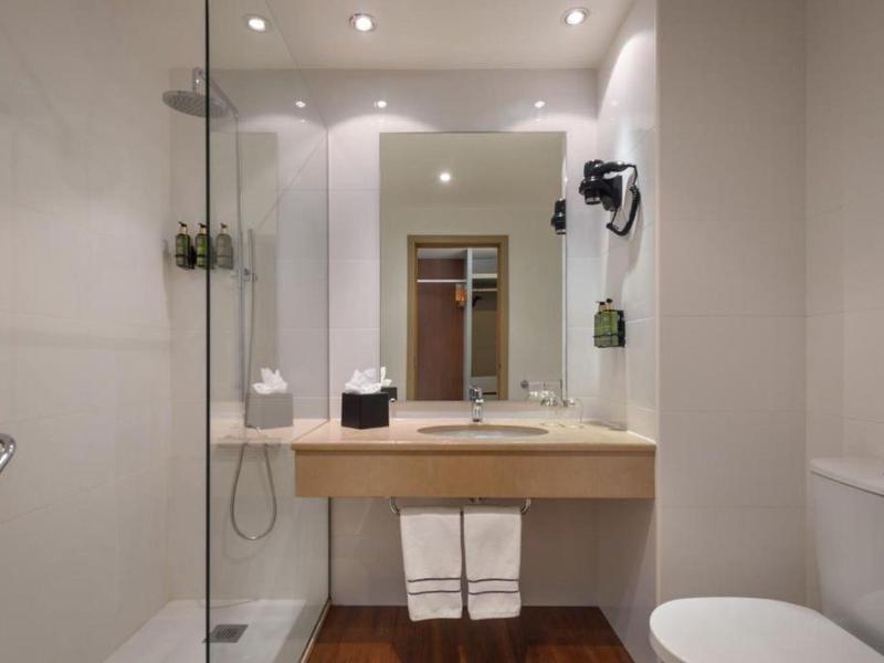 Bagno moderno con doccia, lavabo, specchio e asciugacapelli in una camera d'hotel.